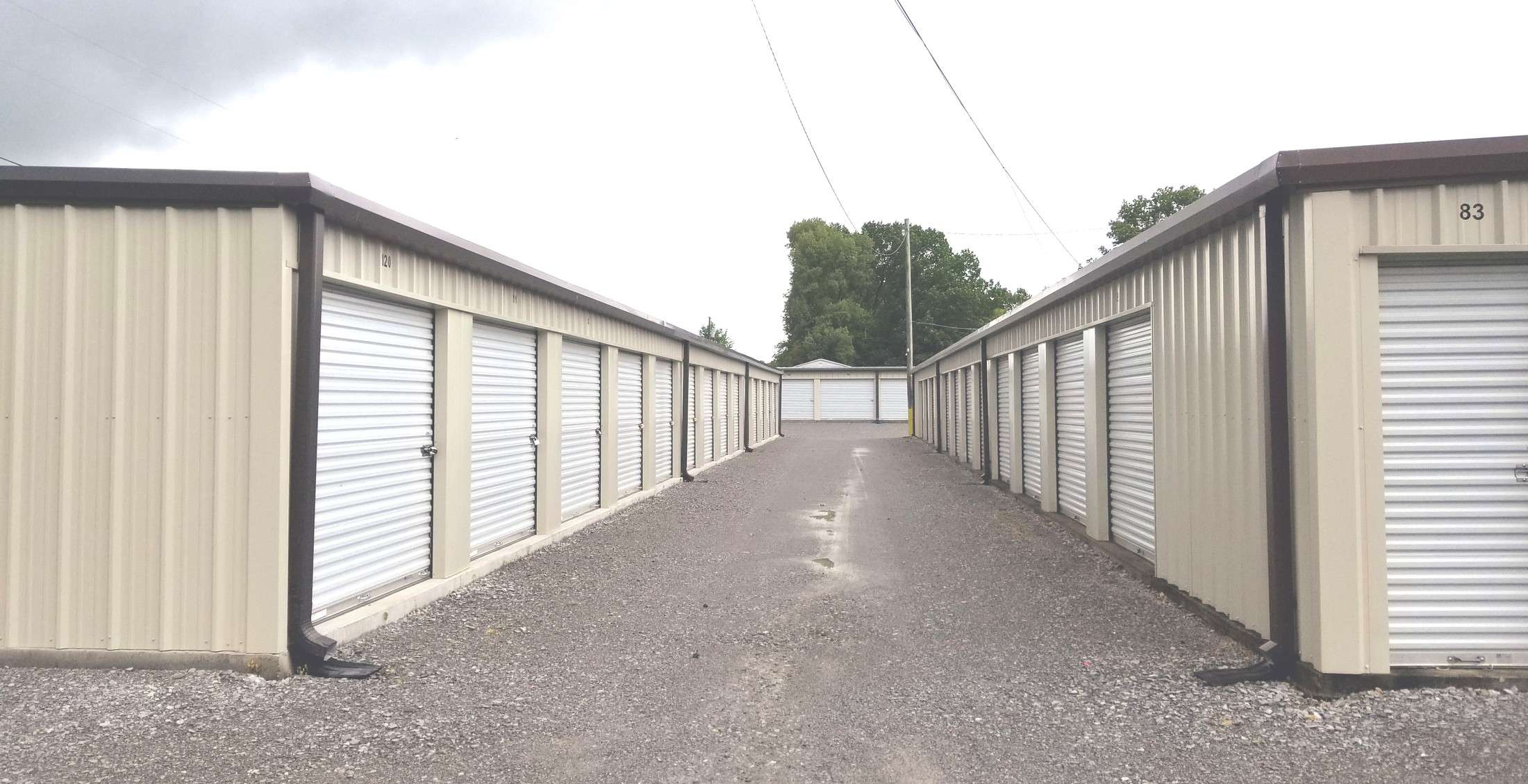Gravel drive between two rows of white roll-up storage units at Loretto Storage